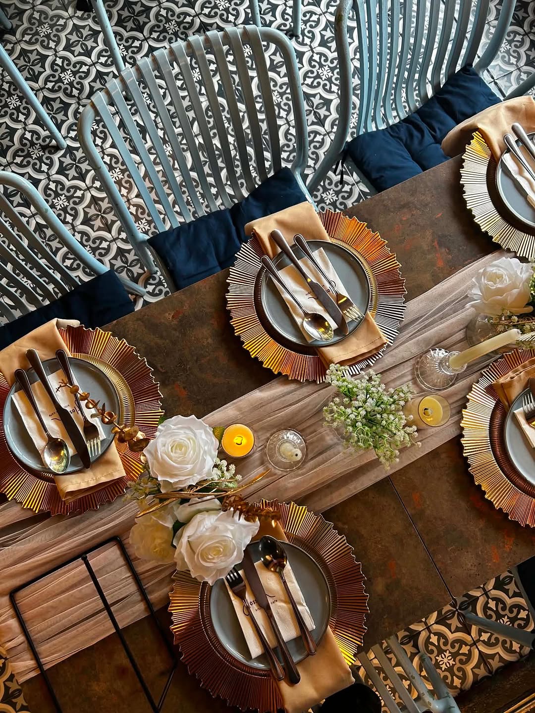 Overhead view of Flossom table setting — gold charger plates and blue rattan chairs